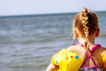 Happy little girl with floaties floaties preparing to swim in the ocean
