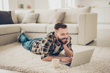 Attractive smiling chill guy is browsing at his laptop, laying o