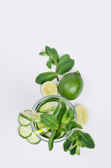 Ingredients for cooking cold green spring drink with cucumber, pieces of lime, fresh leaves mint and ice cubes on soft white background, top view.