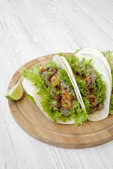 Shrimp tacos on round bamboo board on white wooden table, low angle view. Mexican food.