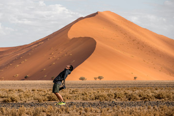 Young male traveler and photographer standing with curve shape in Namib desert with orange sand...
