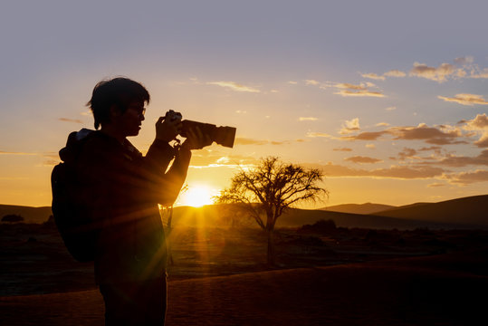 Silhouette shot of male Asian photographer taking photo during the sunrise in Namib desert of Namibia, Africa. Travel photography concept