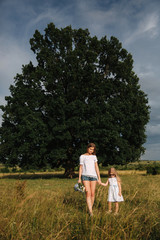 Fototapeta na wymiar Family have fun outside near big tree. Mother and daughter walk though the grass