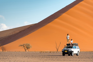 Two Asian man traveler and photographer standing and sitting on camper car near orange sand dune. Travel desert concept © zephyr_p