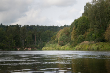 side view on wide still river in forest in summer day with blue sky and clouds