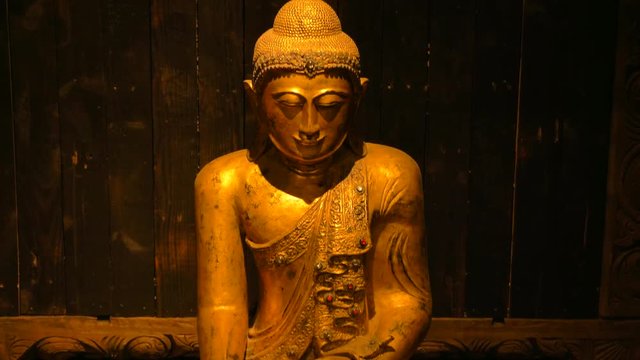 Tilt down shot of a golden Buddha sitting in a wooden lodge.