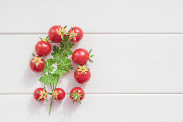 Small fresh red cherry tomatoes with a sprig of green parsley on a light wooden table, top view, copy space
