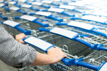 Male hand shopper pulling shopping cart (trolley) from row in supermarket or grocery store. Shopping lifestyle concept