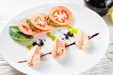 Caprese salad with mozzarella, tomato, basil and balsamic vinegar arranged on white plate