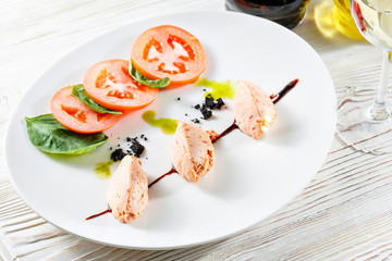 Caprese salad with mozzarella, tomato, basil and balsamic vinegar arranged on white plate