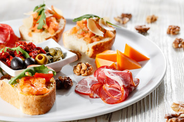 Plate with Italian appetizers. Bruschetta with a cherry tomatoes and shrimps. Parmesan cheese, prosciutto, green capers, olives, sun-dried tomatoes and walnuts.