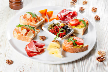 Plate with Italian appetizers. Bruschetta with a cherry tomatoes and shrimps. Parmesan cheese, prosciutto, green capers, olives, sun-dried tomatoes and walnuts.