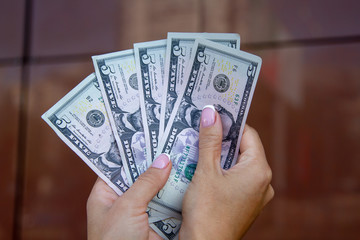 The woman counts the dollar bills, fanning them in her palms against the background of a brown shiny wall. Counting money. Crisp dollar bills close-up.