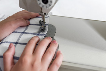 Hands of a seamstress on a sewing machine in the process of sewing with a copy of the space