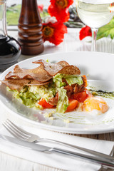 Classical Caesar salad with roasted chicken, poached egg, lettuce leaves, crackers, parmesan and tomatoes and cream sause on the white round plate close up. restaurant menu