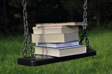 Stos książek leży na dziecięcej huśtawce na łańcuchu w parku