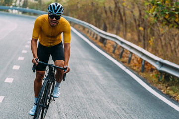 Fototapeta na wymiar Focus on Asian man wearing a yellow cycling jersey, who's riding a road bike up high on hill in the morning. Under morning sunshine with determination on his face.