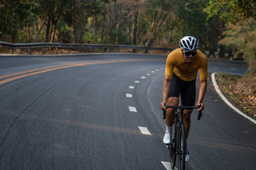 Focus on Asian man wearing a yellow cycling jersey, who's riding a road bike up high on hill in the morning. Under morning sunshine with determination on his face.