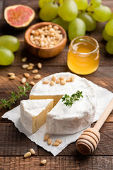 Fototapeta na wymiar Brie or camembert with pine nuts, figs, honey and green grapes on brown wooden serving board. Closeup view, selective focus