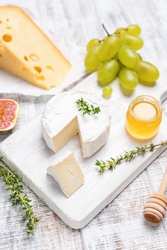 Camembert or brie cheese on white wooden serving board with honey, green grapes, figs and thyme. Top view, selective focus