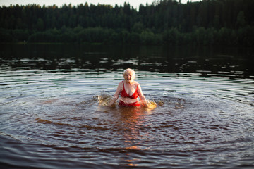 Elderly woman splashes in the summer river at sunset.