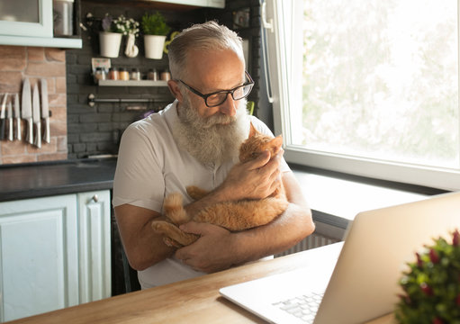 Elderly man with his cat working on laptop, smiling, looking at screen.