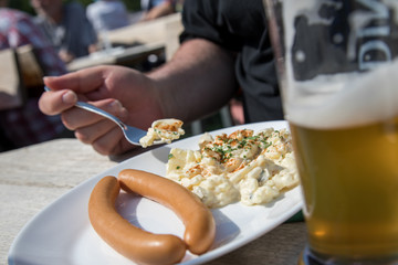 Mann isst ein Paar Wiener Würstchen mit Kartoffelsalat und Bier im Biergarten