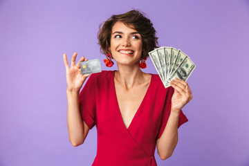 Photo of excited young woman 20s wearing big straw hat smiling while holding credit card and fan of...
