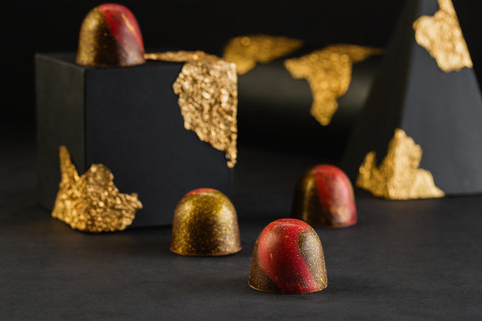 Luxury bonbons with red and gold splashes on black background with geometric figures