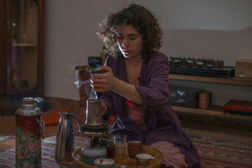 Asian woman with curly hair prepares tea in a dark room