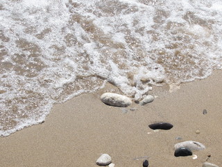 The shore of the sea close-up: a pebble from a pebble with sand and an incident wave. Beautiful background.