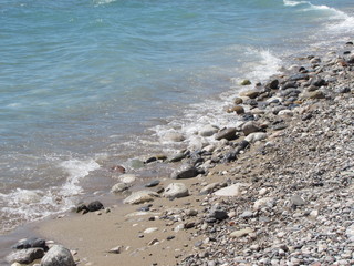The shore of the sea close-up: a pebble from a pebble with sand and an incident wave. Beautiful background.