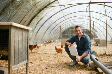portrait of handsome young farmer veterinarian taking care of poultry in a small chicken farm