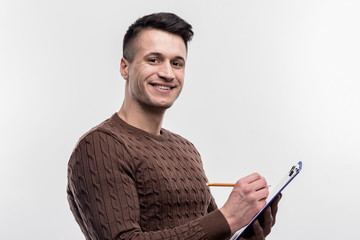 Male secretary. Smiling dark-haired male secretary wearing brown sweater making notes on image...