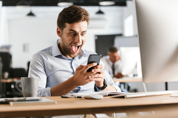 Screaming happy business man using smartphone and rejoices