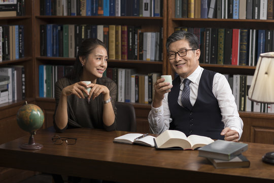Cheerful mature couple talking and drinking tea in study