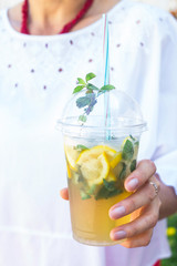 A woman in a white blouse holds a plastic glass with a mojito mug and a mint. Summer drink to cool outside