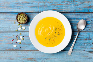 Autumn vegetable or pumpkin soup with seeds in white bowl on wooden turquoise table top view.