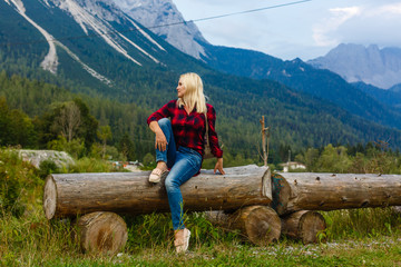 Naklejka premium Young tourist woman is sitting on the top of the mounting and looking at a beautiful sea bay landscape. Hiking woman with backpack relaxing on the top of the cliff enjoying sunlit sea view.
