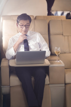 Senior businessman using laptop on airplane