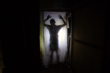 Human silhouette behind packing film in dark creepy room of abandoned building