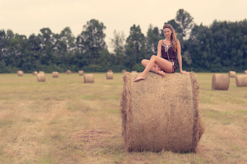 Naklejka na ściany i meble Beautiful woman sitting on hay bale a summer's day