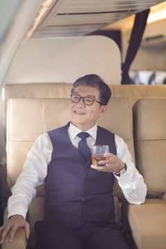 Senior businessman drinking whiskey on airplane