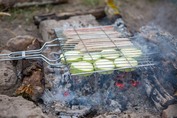 Photo of grill for barbecue with vegetables and sausages on fire in forest