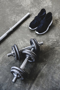 top view of adjustable dumbbells and bar with sneakers on concrete surface