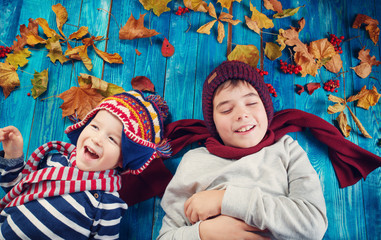 Children in hats and scarfs and maple leaves on blue background