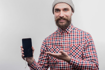 Phone and earphones. Stylish bearded blue-eyed man holding his smart phone and earphones on image...