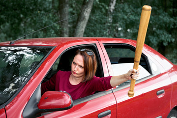 young female driver has stress and anger, threatens with a baseball bat, has a red car
