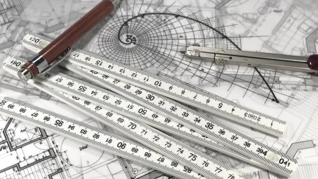workplace of the architect: architectural drawings - blueprints, yardstick - folding ruler, a pencil and compass smoothly rotate on the surface of the architectural plan of a modern house