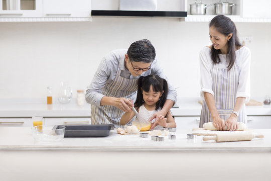 Happy little girl and grandparents baking cookies in kitchen